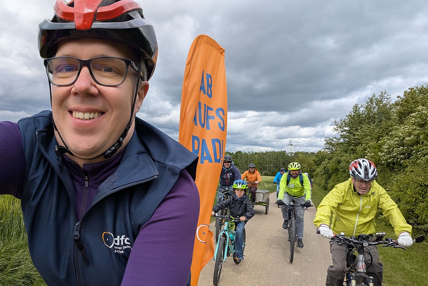 Unterwegs über die Felder auf dem Weg nach Weil der Stadt Ein Foto von der Radtour unterwegs: Ein Radler fährt mit Beach Flag "Ab aufs Rad!" voraus, dahinter folgt die Gruppe.